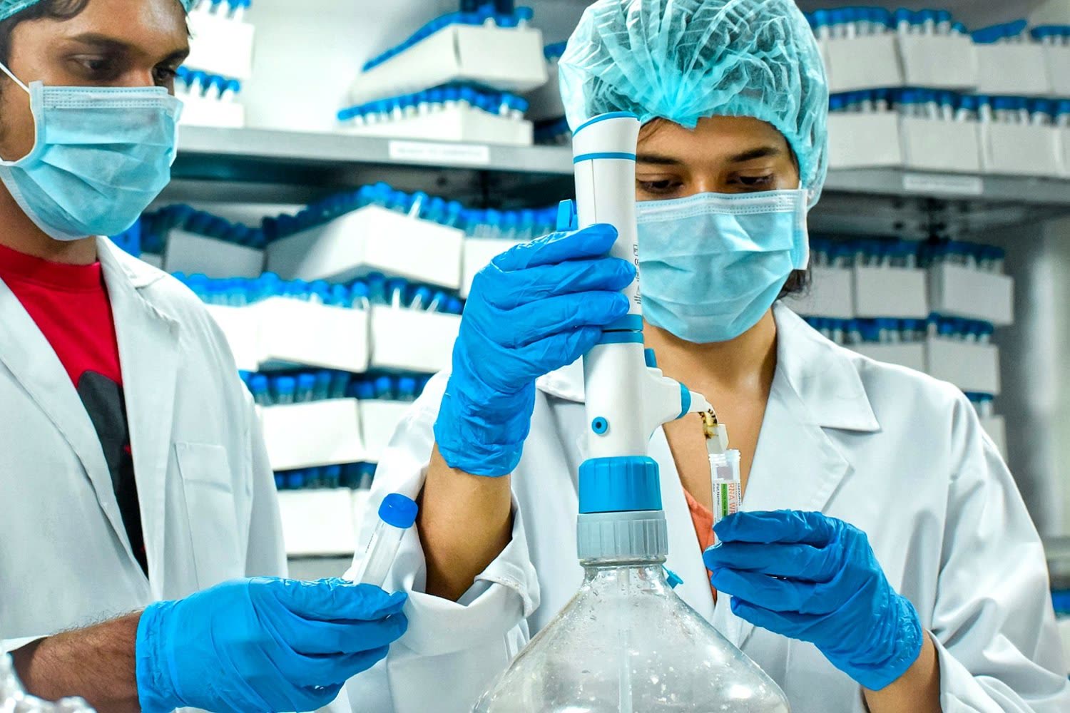 Two Azooka scientists in hairnets and masks examining a reagent bottle